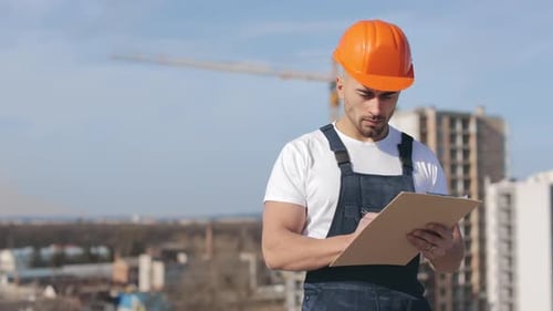 The Engineer is Writing Data to Work Documents and Looking Seriously at the Camera