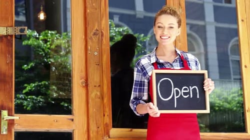 Smiling waitress standing outside door with open sign board in cafe
