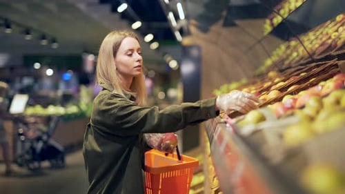 young blonde woman picks chooses fruits vegetables on the counter in supermarket.