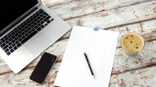 Coffee cup, laptop, mobile phone, clipboard, pen on wooden plank