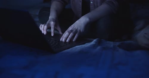 Hands Typing on Laptop in Dimly Lit Room