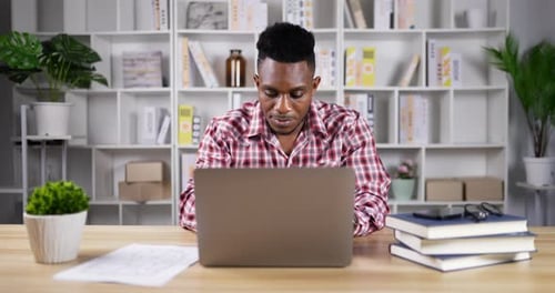 Young Man Works on Laptop at Home Office Desk