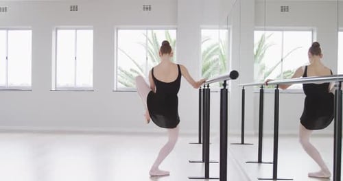 Caucasian female ballet dancer stretching up by the mirror in a bright studio