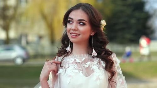 The Bride in a White Dress Shows Beautiful Makeup on Her Face in the Street