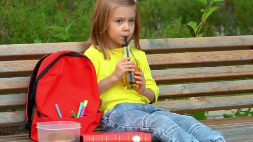 Girl Drinks Refreshment on Park Bench After School