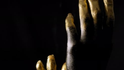 Nahaufnahme der Hände einer jungen Frau in schwarzer und goldener Farbe auf der Haut im Dunkeln