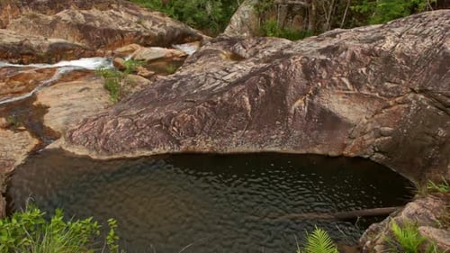 View of Deep Oval Pool Among Rocks Against Foamy Stream