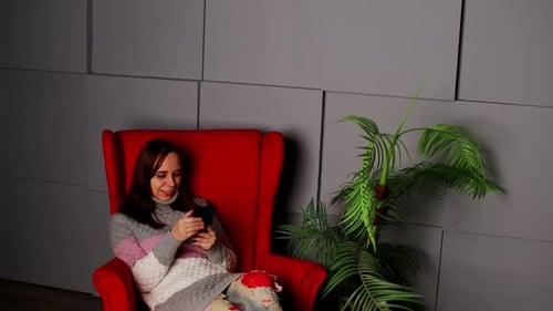 Woman Relaxing in Armchair Using Smartphone Indoors