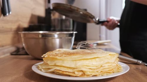 Stapel Pfannkuchen auf dem Hintergrund einer unkenntlichen Frau, die Teig in eine Bratpfanne gießt