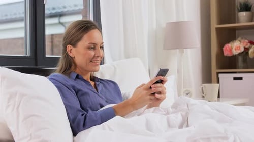 Smiling Woman Using Phone While Lying in Bed