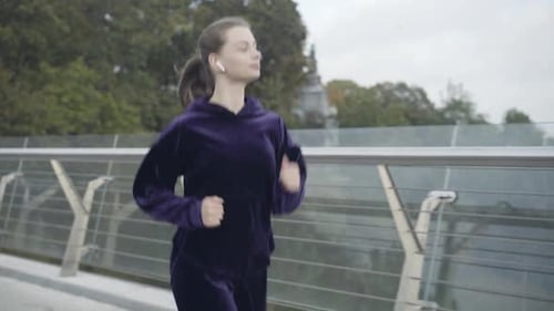 Portrait of Happy Young Sportswoman in Earphones Running on Bridge Outdoors