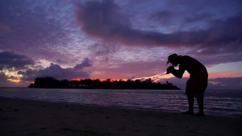 Un habitant de l'île souffle une conque au coucher du soleil sur une île tropicale pittoresque des Fidji.