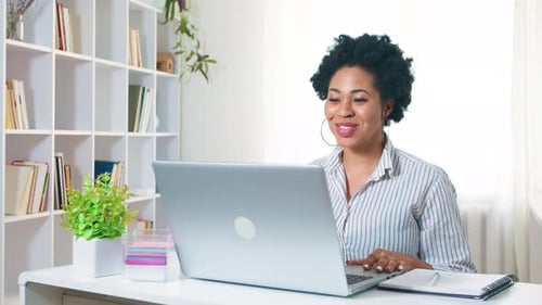 Smiling Woman Video Conferencing on Laptop at Desk