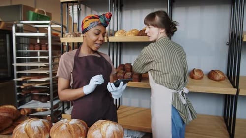 Two Diverse Female Colleagues Using Tablet while Working in Bakery
