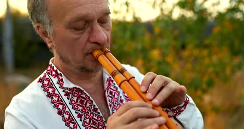 Großes Porträt eines männlichen Musikers in einem ukrainischen Volkskostüm, der auf einer hölzernen Pfeife spielt
