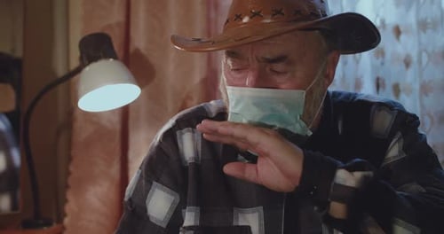 Elderly Man Coughing Wearing a Cowboy Hat and Mask
