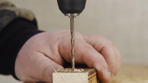 Artisan Holds Board and Drills It with Drill Into Screwdriver Closeup Side View