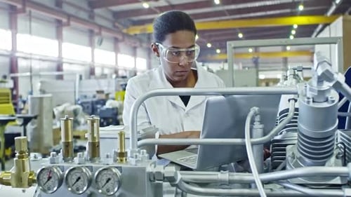 Afrikanische Ingenieurin bedient Industriemaschine mit Laptop