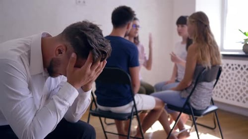 Man Covering Face in Group Therapy Session