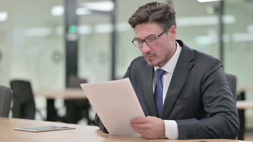 Middle Aged Businessman Reading Documents in Office