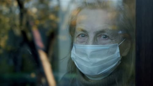 Senior Woman Wearing Mask Looking Through Window