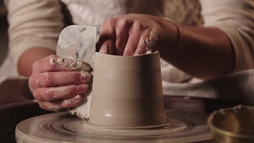Atelier de poterie Jeune femme potière lissant les côtés du pot à l'aide d'un outil