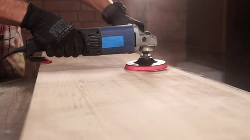 Nahaufnahme der Hände eines Mannes, der mit einer elektrischen Bohrmaschine einen Tisch schleift