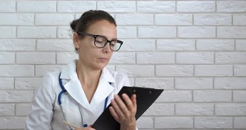 Medical Professional Presents Blank Clipboard Against Brick Wall