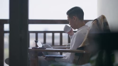 Nervös gestörter junger asiatischer Mann trinkt Kaffee und tippt auf Laptop-Tastatur