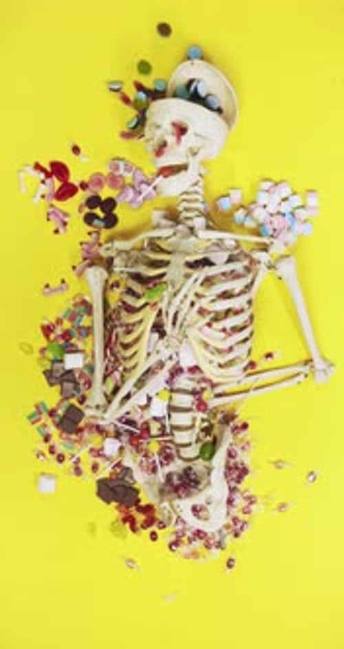 Skeleton Surrounded by Colorful Candies on Yellow Background