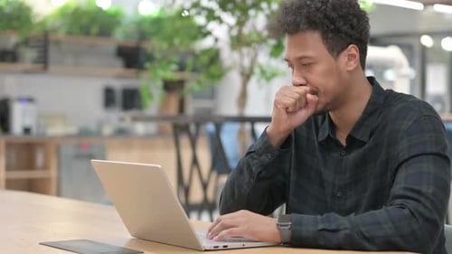 Man Coughing While Working at a Laptop