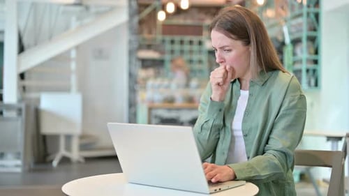 Sick Young Woman with Laptop Coughing in Cafe