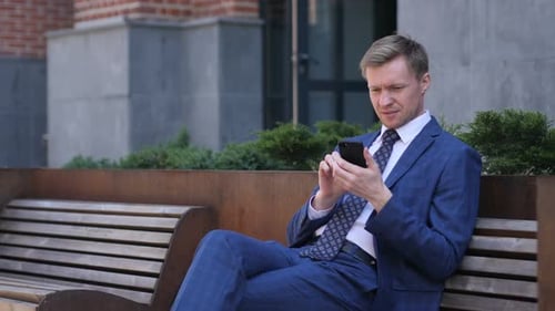 Man in Suit Using Phone on Bench Downtown