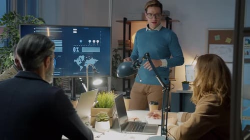 Businessman Making Presentation Using Digital Screen Speaking to Group of Colleagues in Dark Office