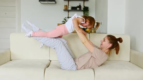 Mother Lifts Child During Playful Workout on Sofa