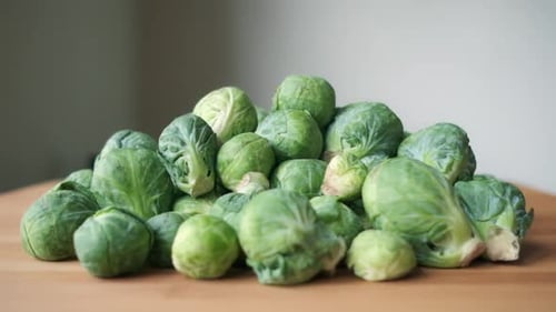 Brussels Sprouts Falling In Slow Motion onto Heap on Light Wood Cutting Board, Slight Push-In Moveme