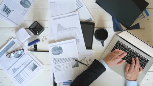 Top View Hands of Young Entrepreneur Typing Text on Laptop Keyboard at White Desk in Office