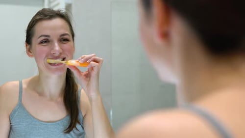 Young Woman Brushing Teeth in Bathroom Mirror