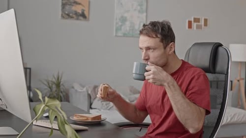 Mann frühstückt während der Arbeit am Computer