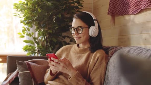 Fröhliche Frau hört Musik und benutzt Smartphone zu Hause