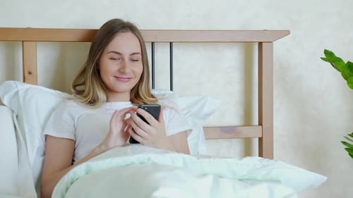 Smiling Woman Using Smartphone in Bed