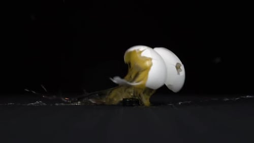 Ein Schuss in ein Hühnerei aus einer pneumatischen Pistole. Ein weißes Ei bricht aufgrund einer Aufnahme auf schwarzem Hintergrund