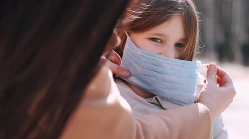 Woman Helping Girl with Face Mask Outdoors