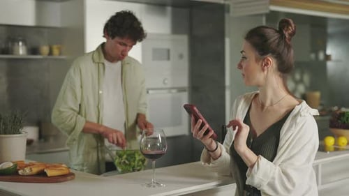 Homem cozinhando na cozinha enquanto mulher usa telefone celular