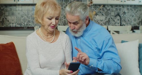 Senior Couple Using Smartphone Together on Couch