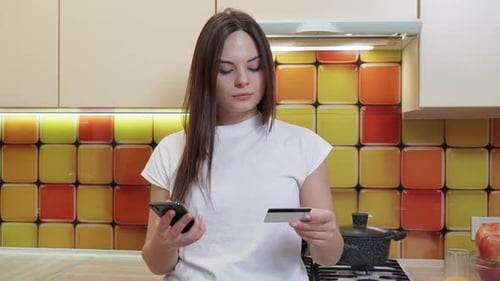 Woman makes online purchase on phone in kitchen