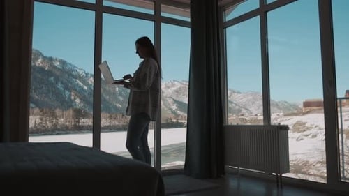 Freiberuflerin arbeitet mit Laptop, während sie am Fenster steht