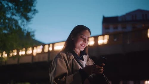 Young woman laughing while typing into her phone at night