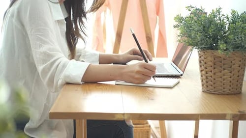 young smiling Asian woman working on laptop while at home in office work space.
