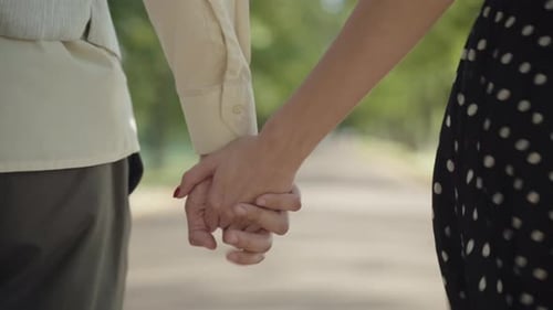 Back View of Unrecognizable Young Couple Walking Along Sunny Alley in Summer Park Holding Hands